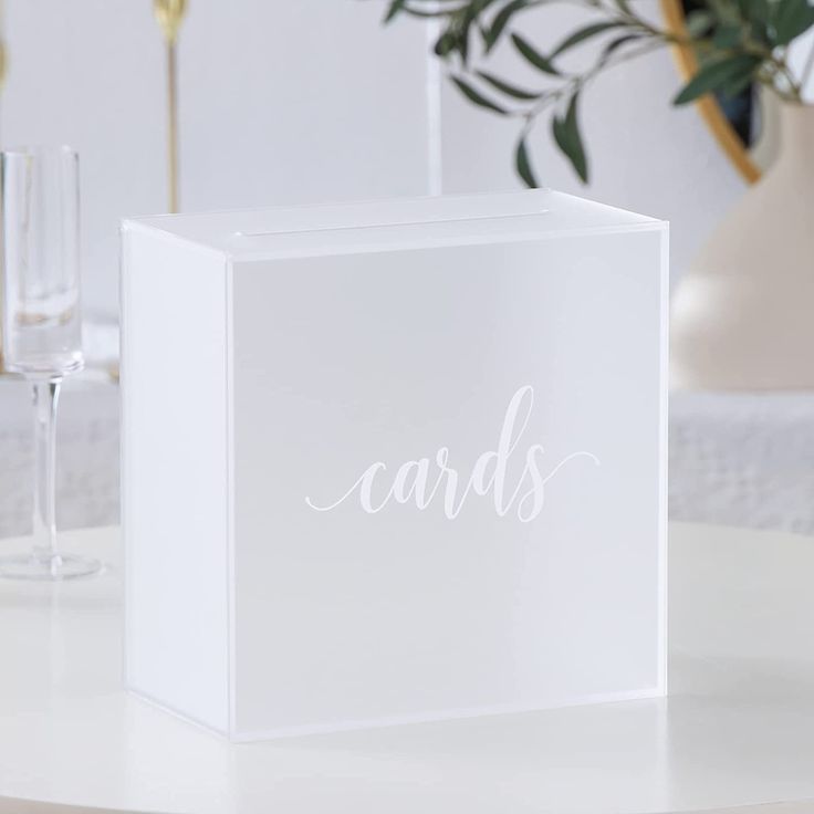 a white card box sitting on top of a table next to a glass filled with wine