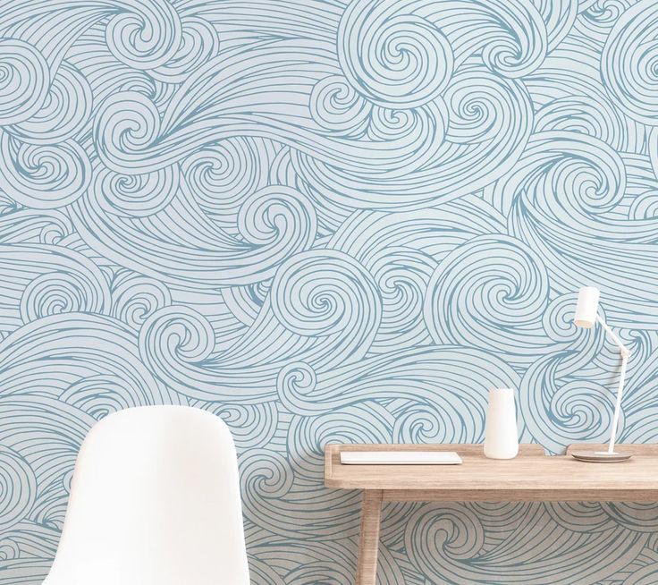 a white chair sitting next to a wooden table in front of a blue wallpaper