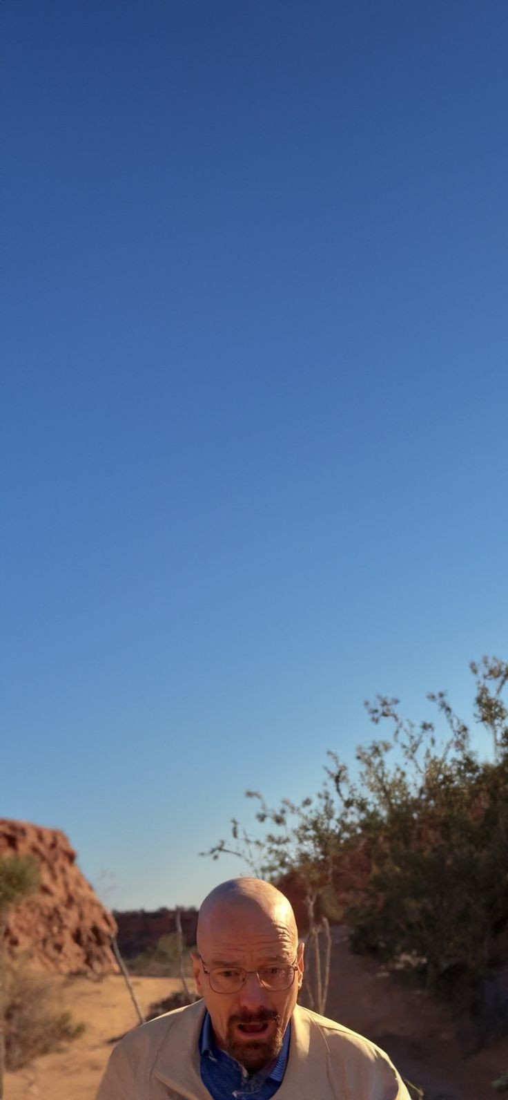 an old man is sitting in the desert looking at his cell phone while he looks off into the distance