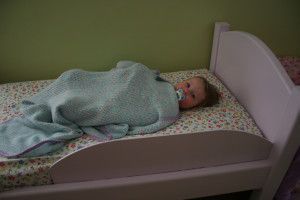 a baby wrapped in a blanket laying on top of a wooden bed with pink and green sheets