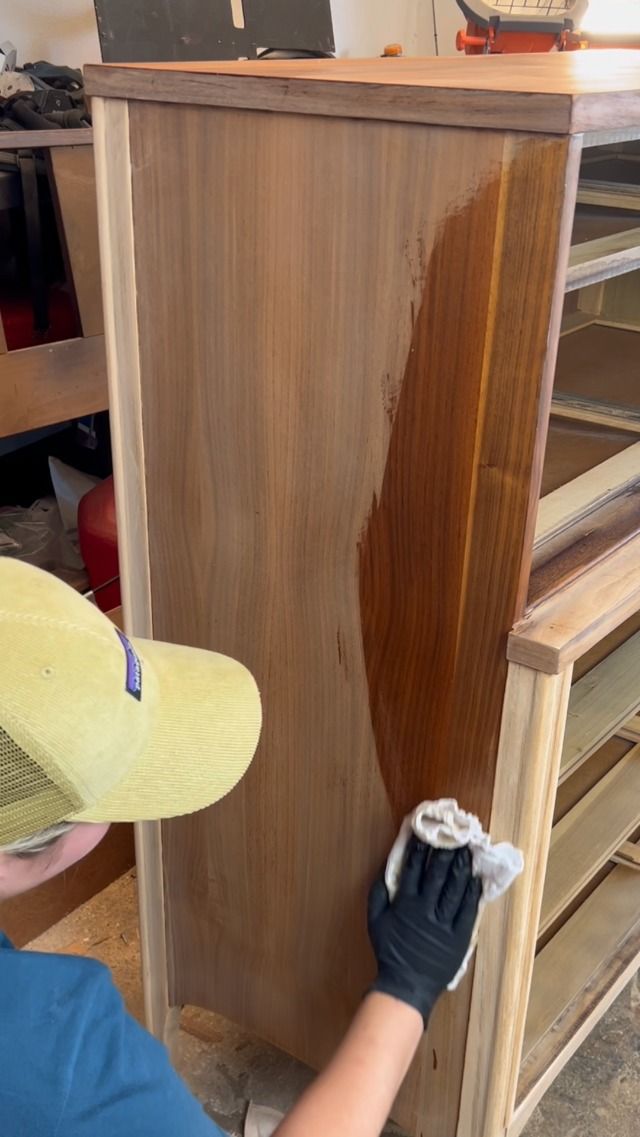 a person with a hat and gloves cleaning a wooden cabinet in a room that is being worked on