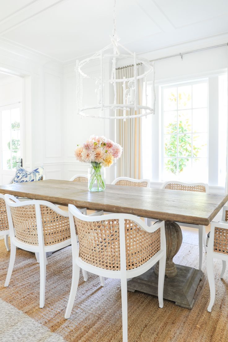 a dining room table with wicker chairs and flowers in a vase on the end