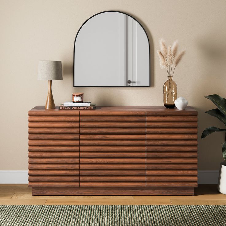 a wooden dresser sitting next to a mirror on top of a wall near a lamp