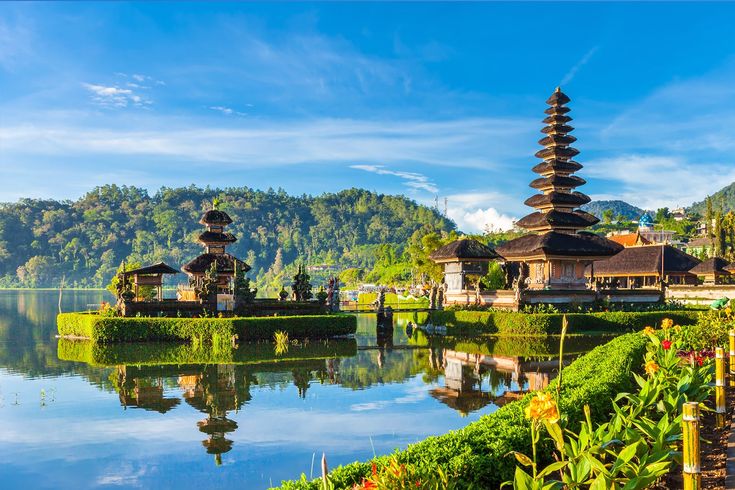 a lake surrounded by lush green plants and tall pagodas in the distance with mountains in the background