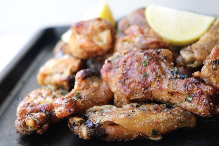 chicken wings and lemon wedges on a black tray