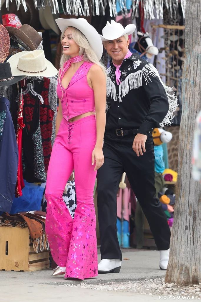 a man and woman in cowboy hats standing next to each other on the sidewalk near clothing racks