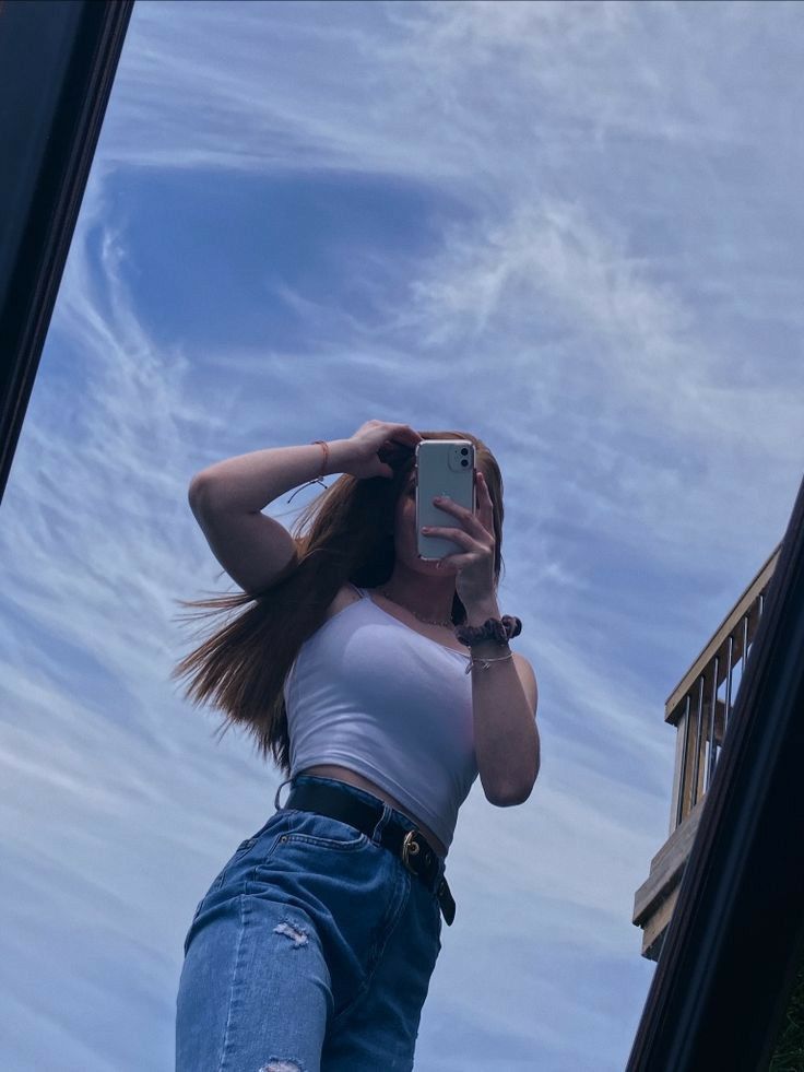 a woman taking a selfie with her cell phone in front of a building and blue sky