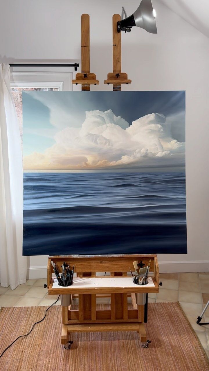 an easel sitting on top of a wooden table in front of a large painting