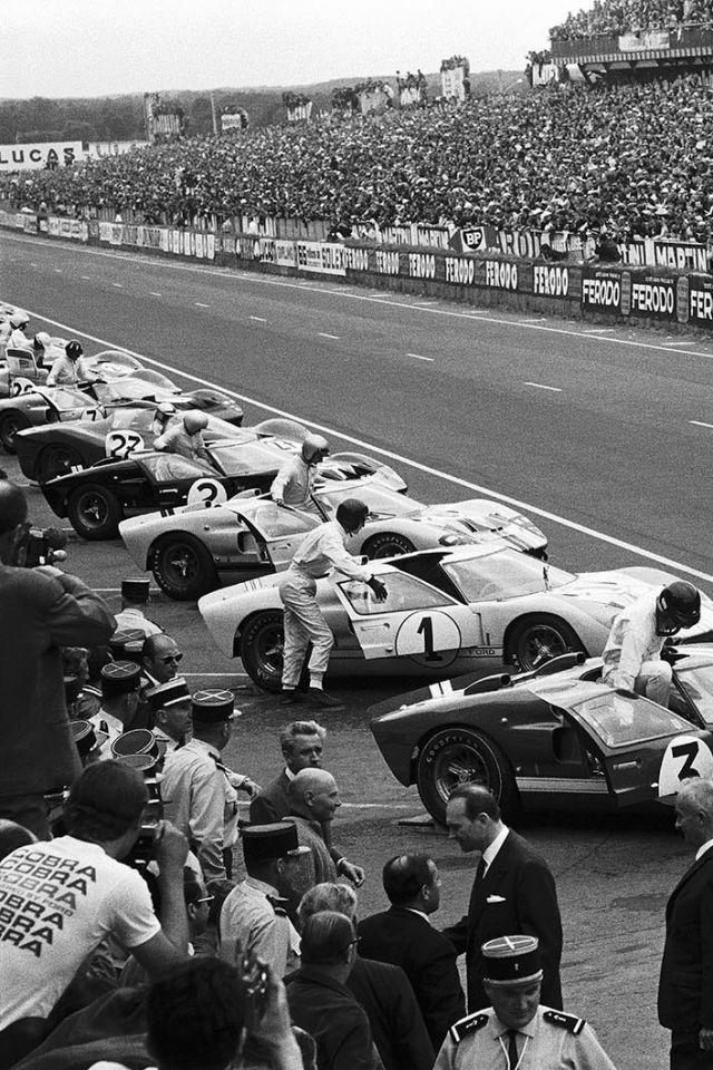 a group of men standing next to each other on top of a race track in front of a crowd