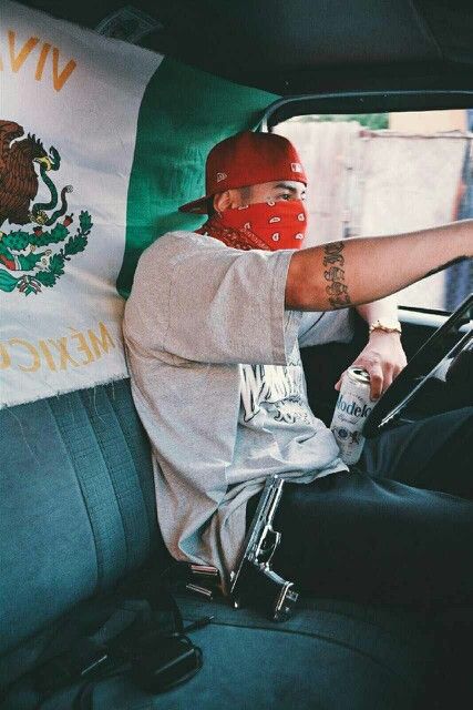 a man wearing a red helmet and bandana drives in a car with mexican flags behind him