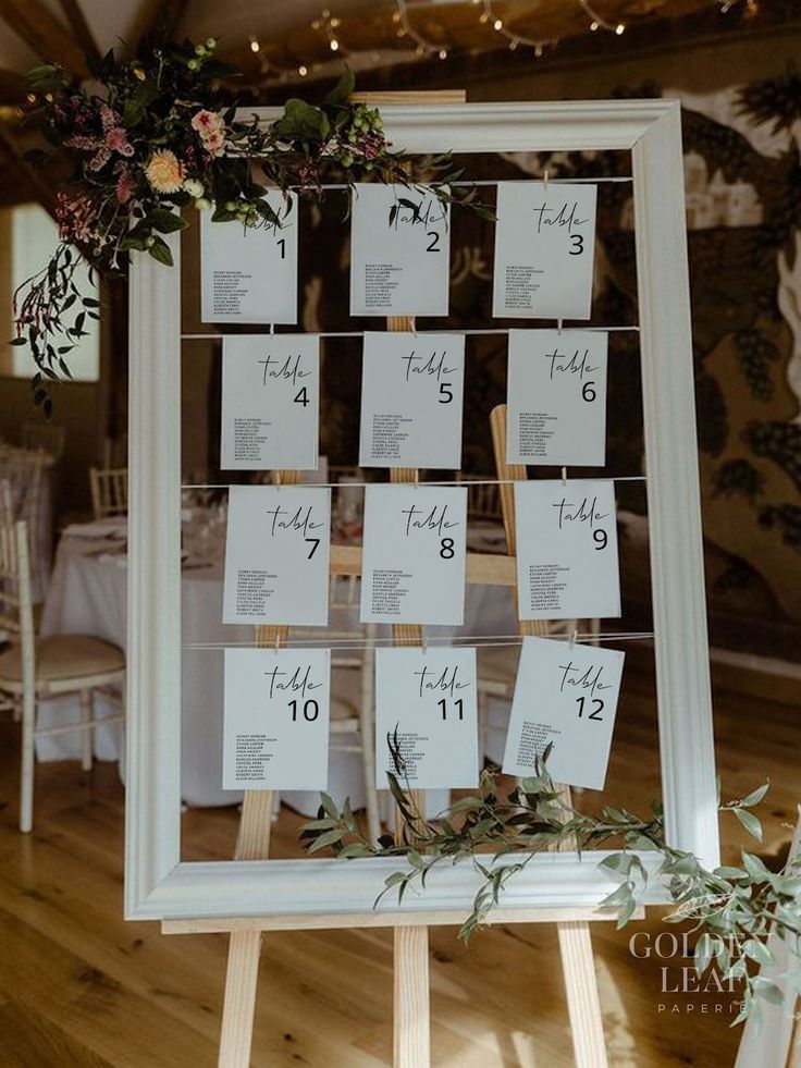 a table with place cards on it and flowers hanging from the wall above them, along with greenery