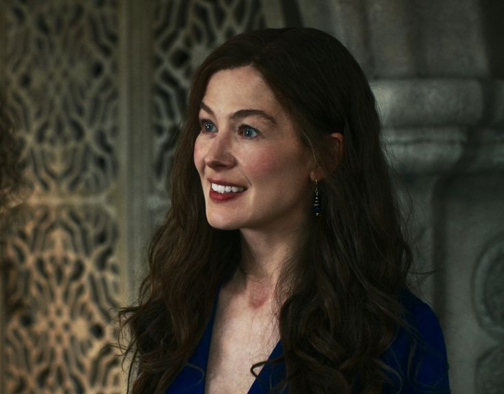 a woman with long dark hair wearing a blue dress and smiling at someone in the background