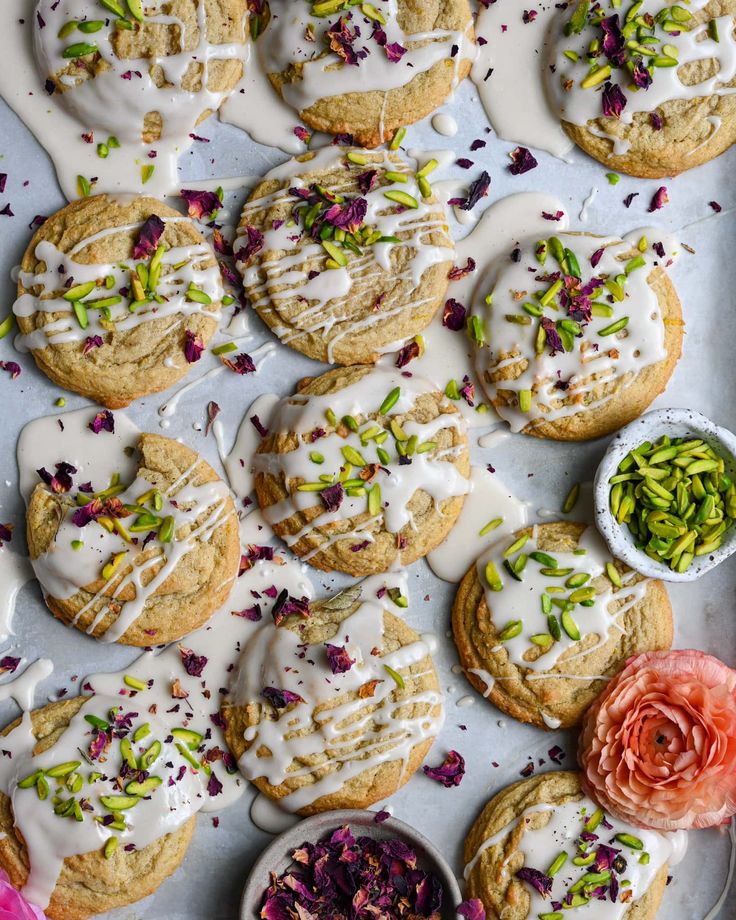 cookies with white icing and colorful flowers on a baking sheet next to small bowls of sprinkles