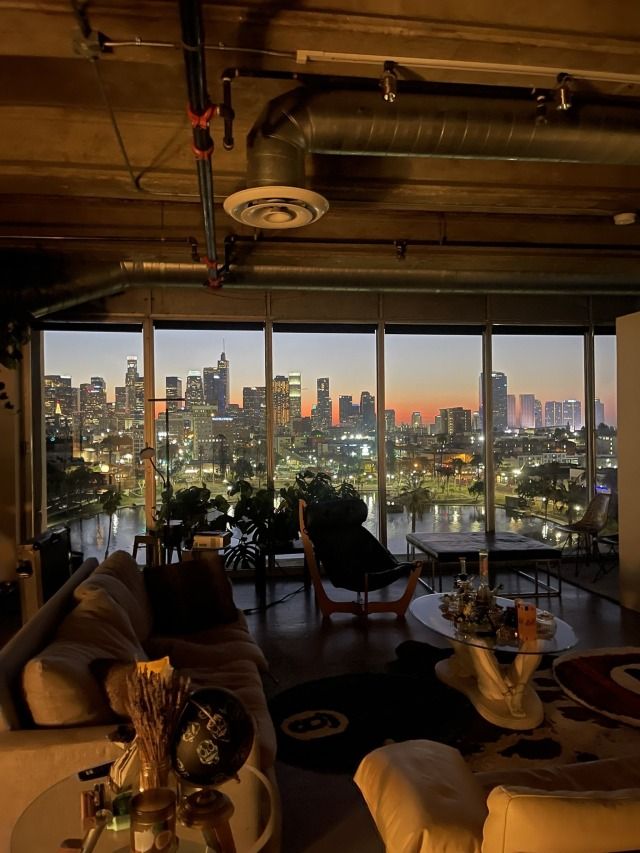 a living room filled with furniture and large windows overlooking a cityscape at night