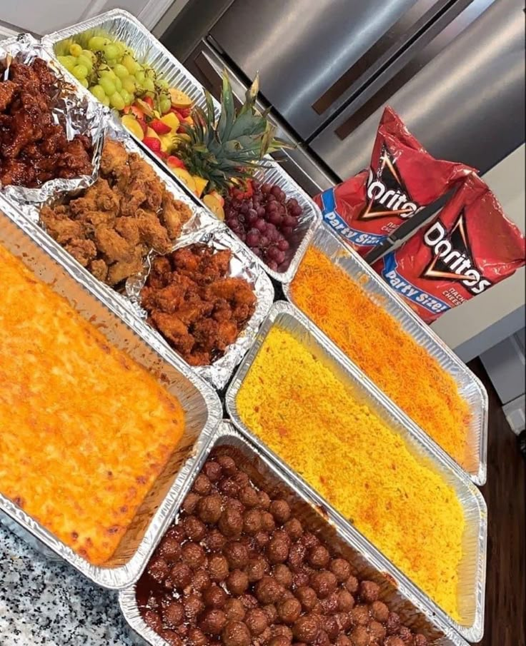 several trays of food sitting on top of a counter next to a bag of chips