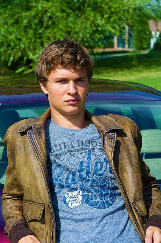 a young man standing in front of a car wearing a leather jacket and t - shirt