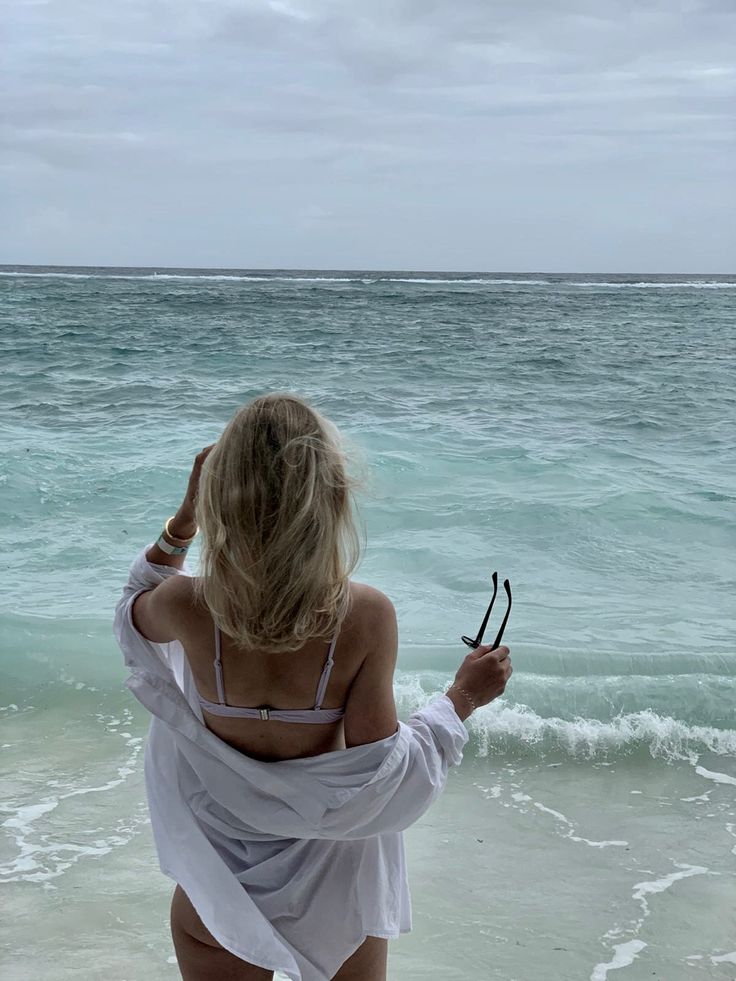 a woman standing on top of a beach next to the ocean holding two pairs of scissors