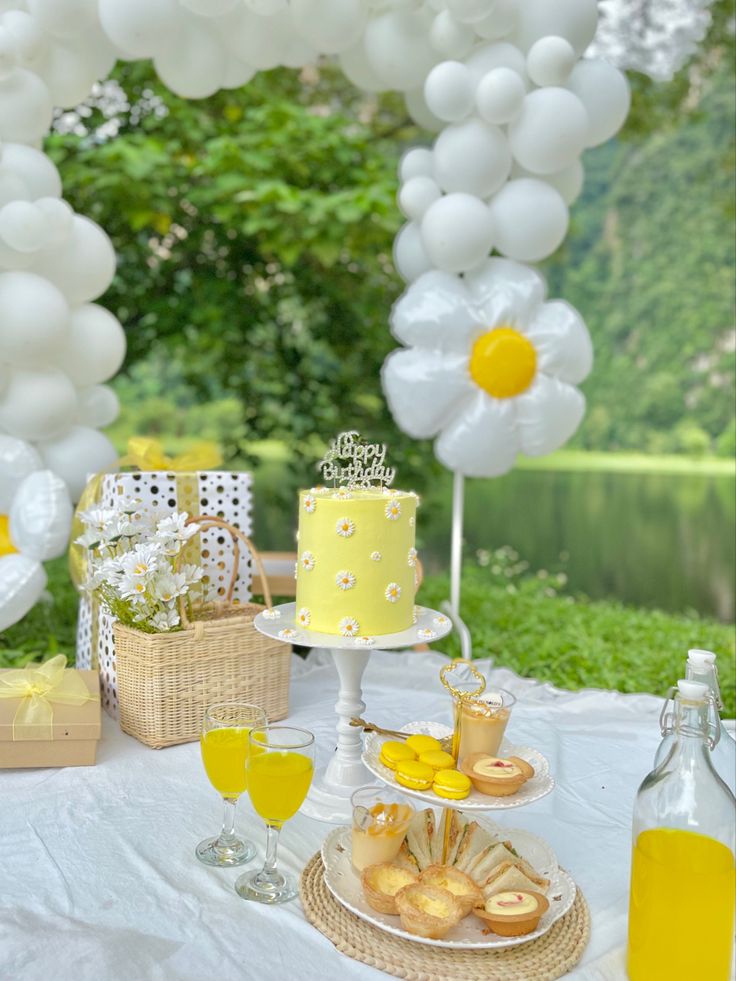 a table topped with a yellow cake and lots of balloons