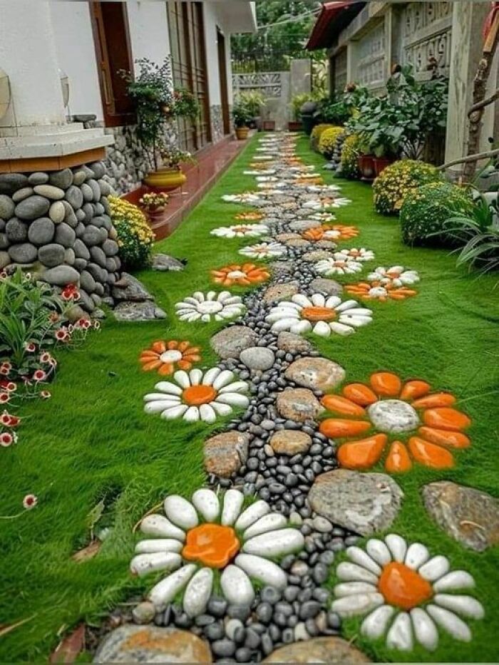 a garden with rocks and flowers painted on the grass, in front of a house