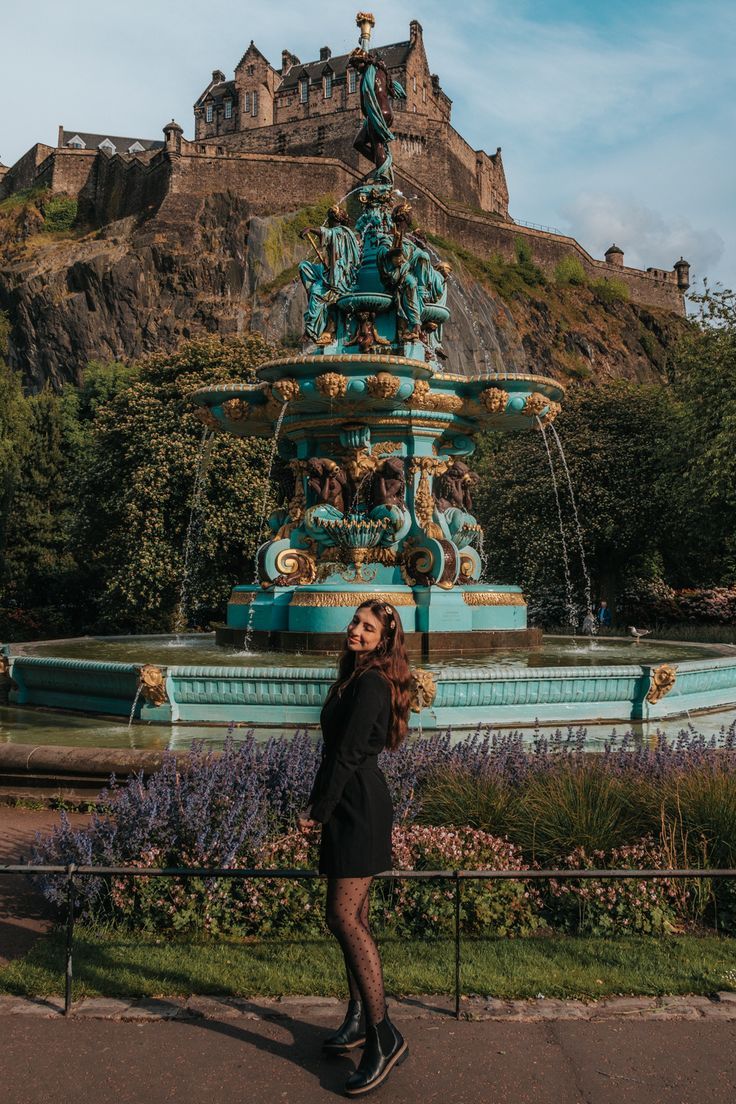 a woman standing in front of a fountain with a castle on the hill behind her