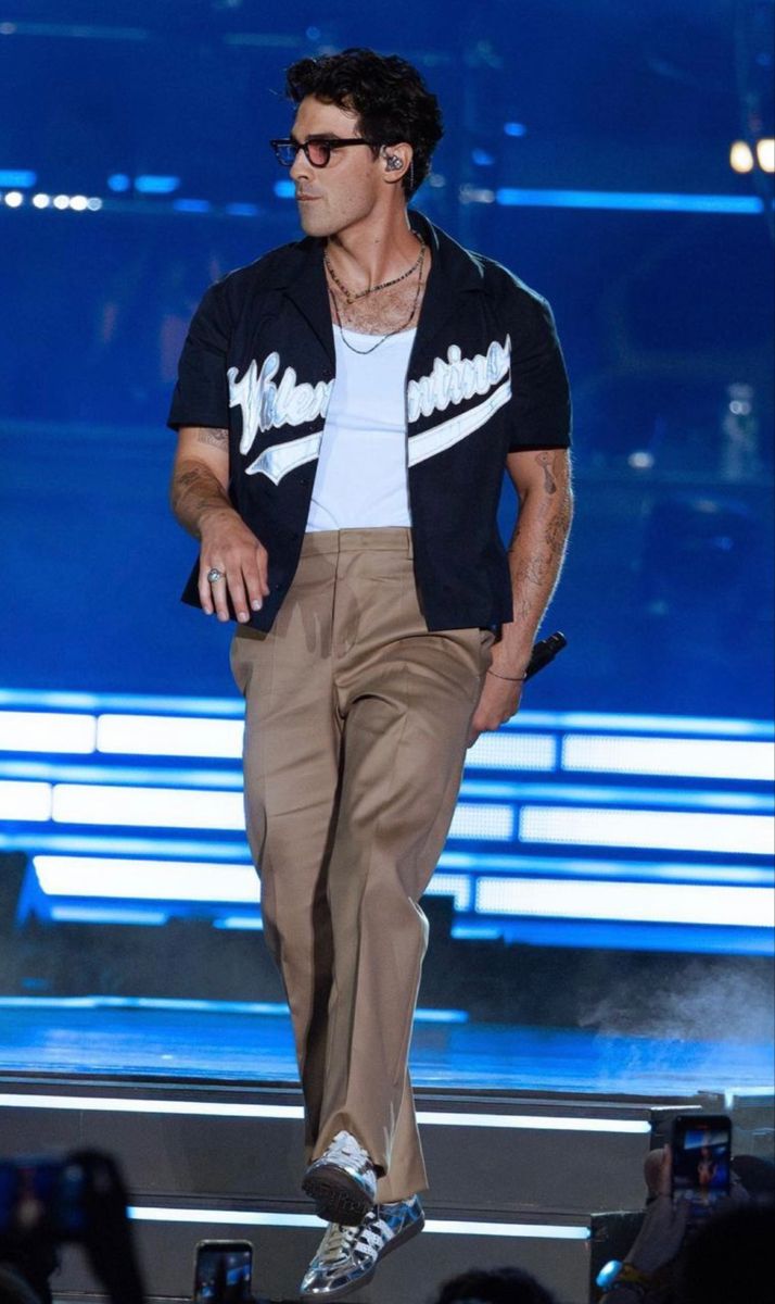 a male in a white shirt and tan pants is on stage with his hands in his pockets