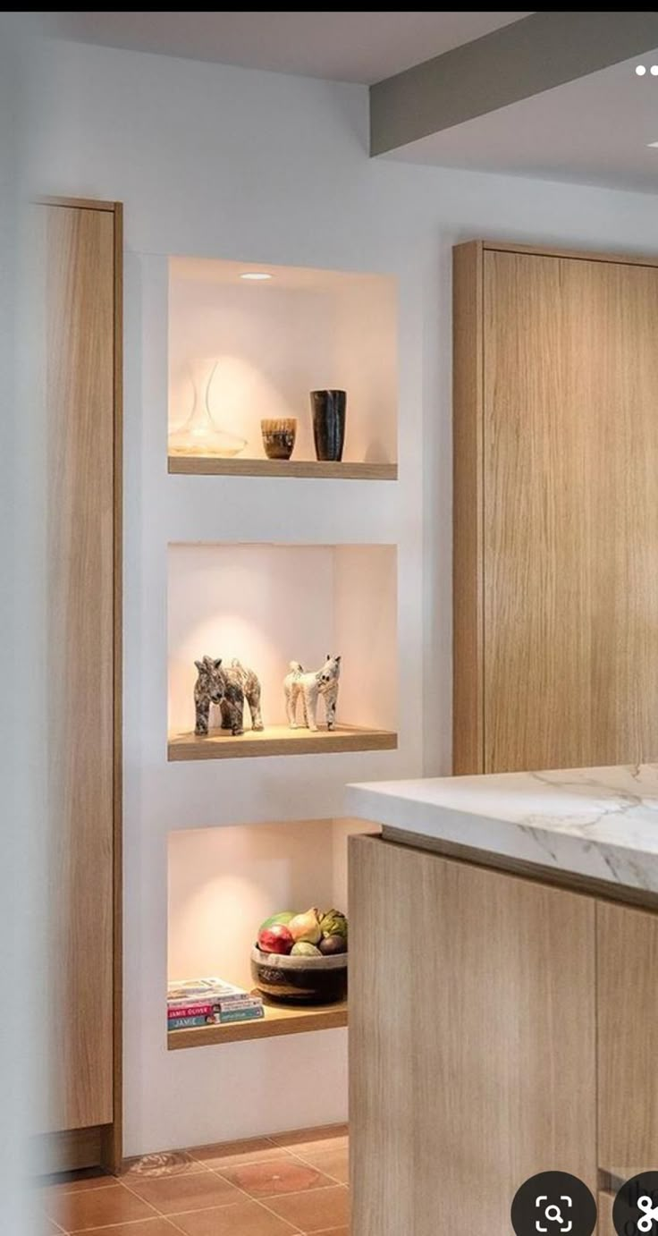 a kitchen with wooden cabinets and marble counter tops, along with shelves filled with vases