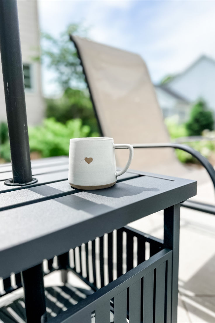 a coffee cup sitting on top of a table next to a metal fence and chair