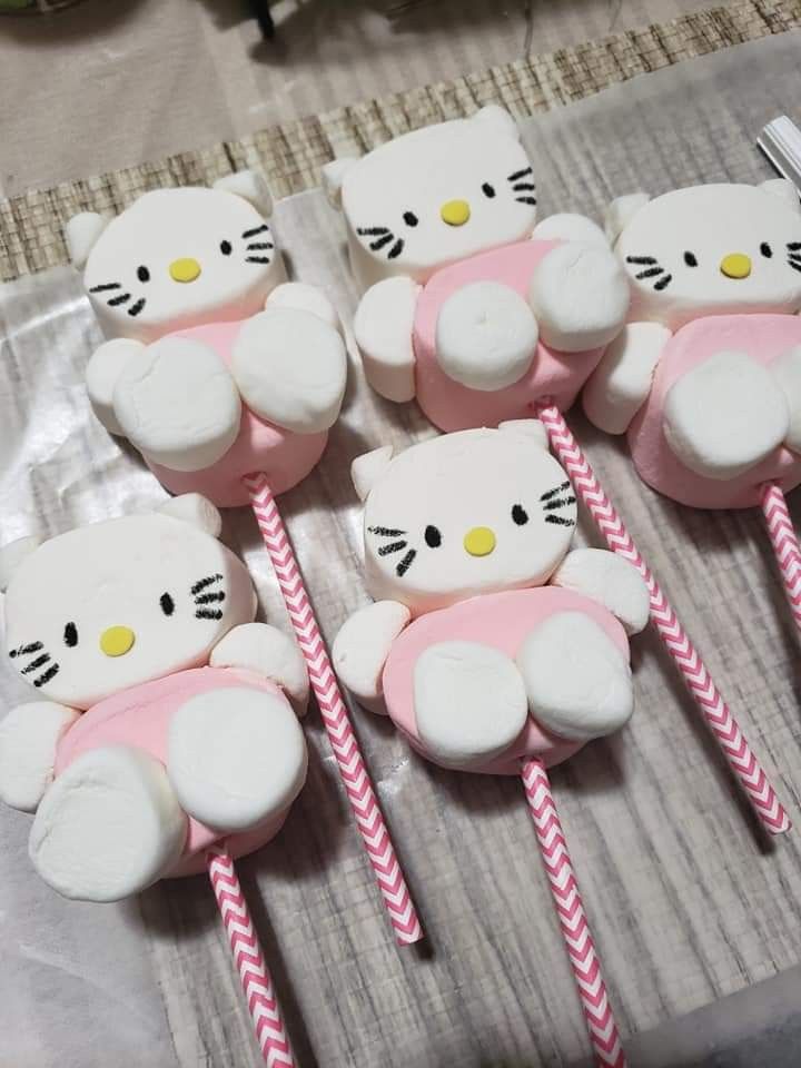 hello kitty cupcakes with pink and white frosting are on a table next to candy sticks