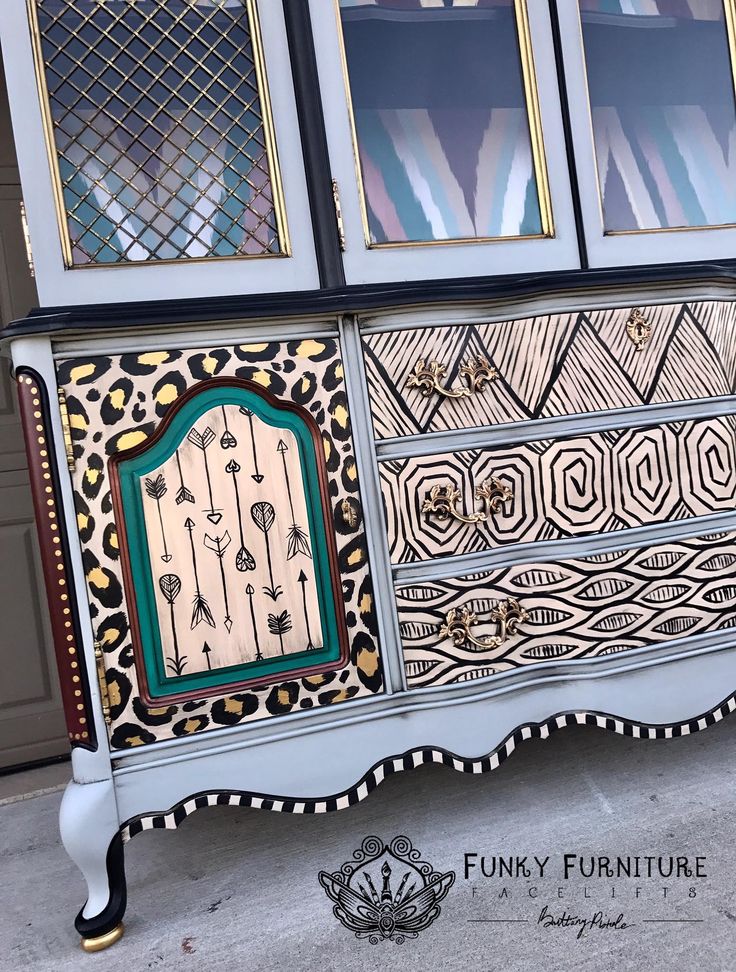 an ornate painted dresser with glass doors and drawers on the top, sitting in front of a garage door