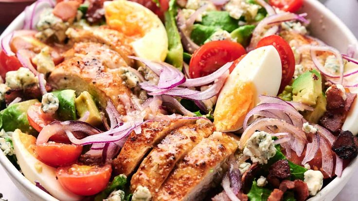 a salad with meat, tomatoes, onions and other vegetables in a white bowl on a table