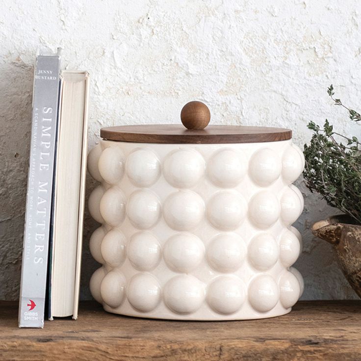 a white container sitting on top of a wooden table next to a book and plant