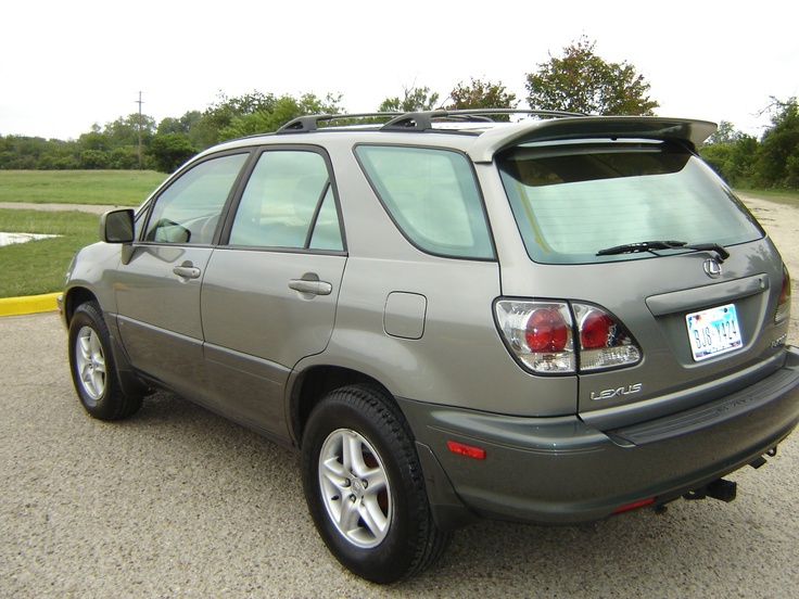 the back end of a silver car parked in a parking lot next to a field