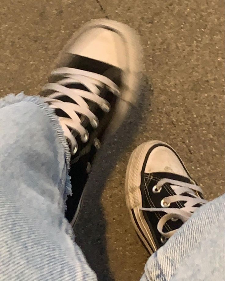 someone wearing black and white converse shoes standing next to each other