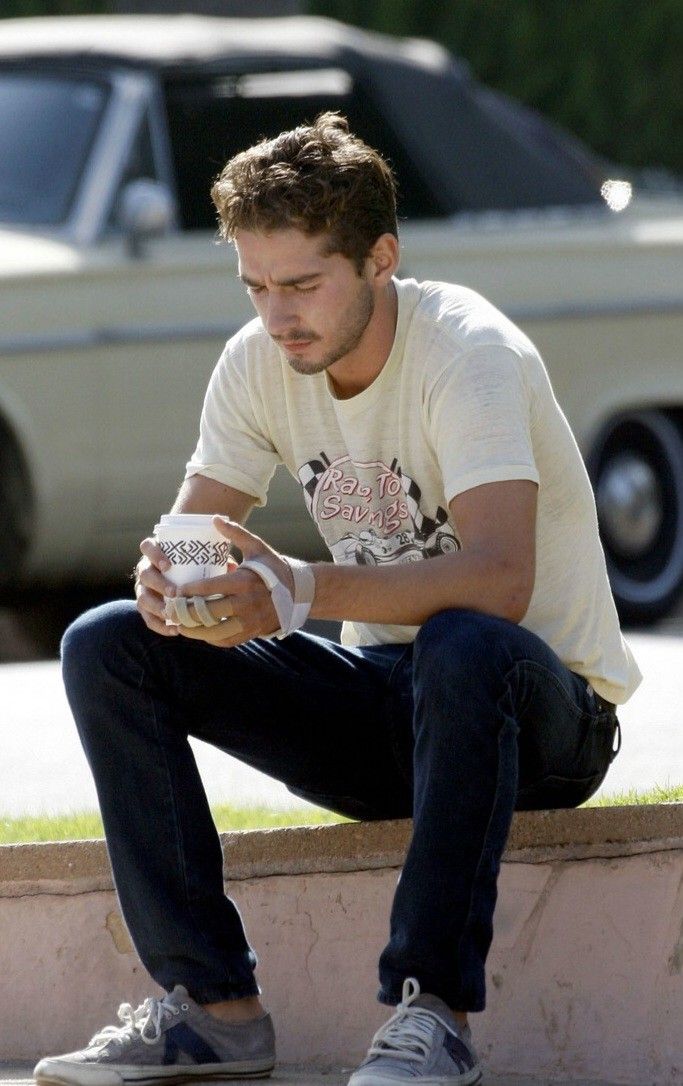 a young man sitting on a ledge holding a cup