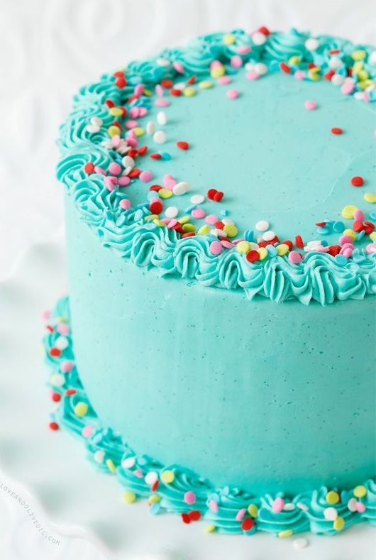 a blue frosted cake with sprinkles is on a white tablecloth