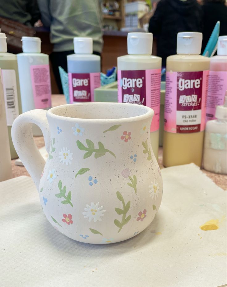 a white vase with flowers painted on it sitting next to some other bottles and containers