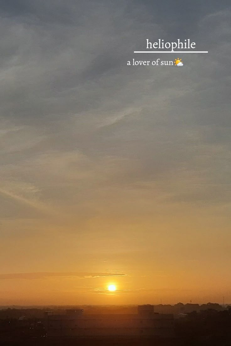 the sun is setting over a field with buildings in the foreground and clouds in the background