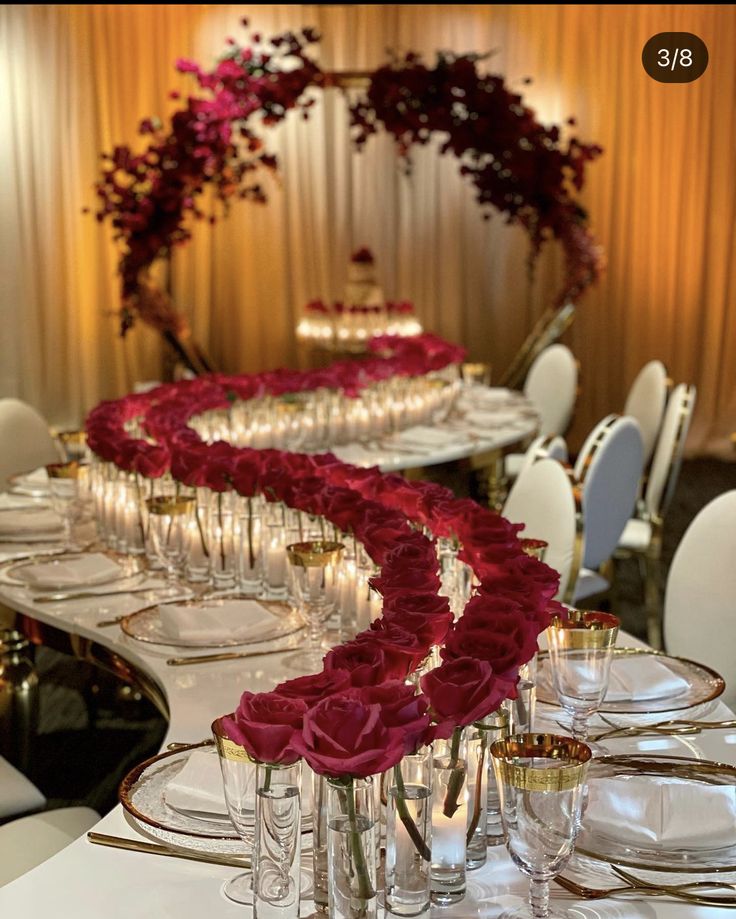 a long table is set with wine glasses and red roses on the centerpieces