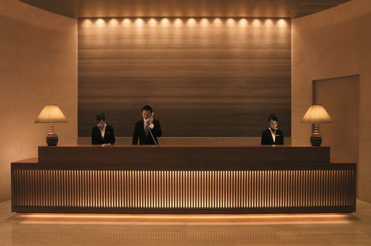 three people sitting at the front desk of a hotel lobby with lamps on either side