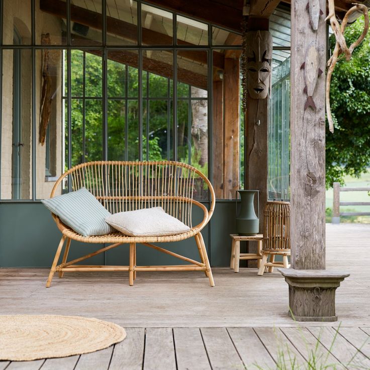 a wicker chair sitting on top of a wooden floor next to a tree in front of a building