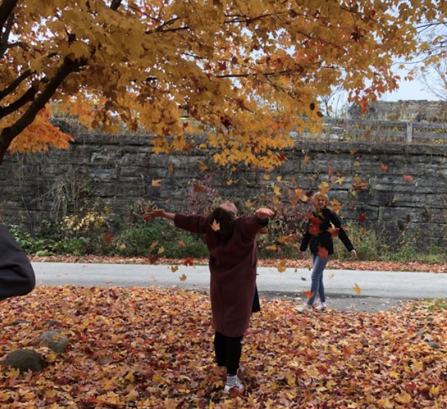 two people are throwing leaves in the air while another person is walking on the sidewalk