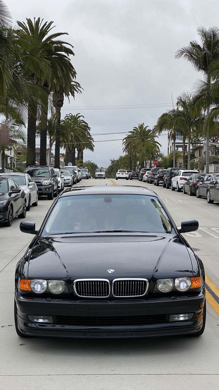 a black car parked on the side of a road next to palm tree lined street