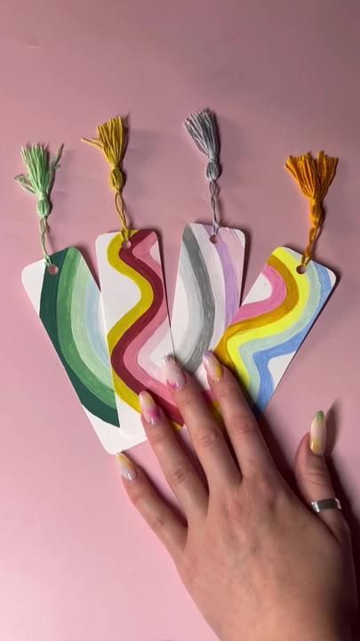 a person's hand is holding four colorful cards with tassels on them