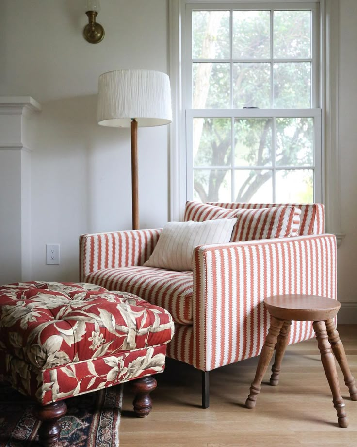 a red and white striped chair sitting in front of a window next to a foot stool