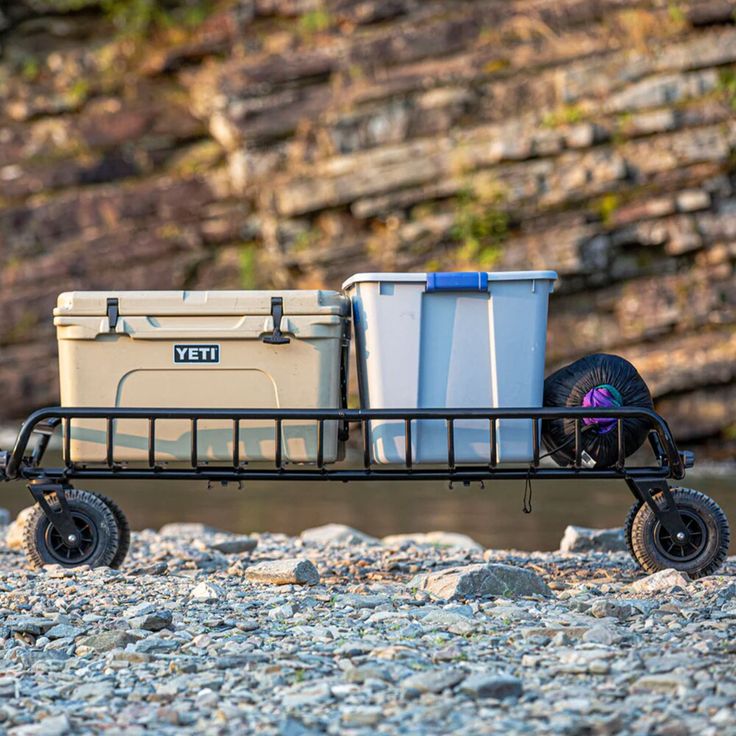 two coolers are sitting on the back of a cart with wheels and tires in front of some rocks