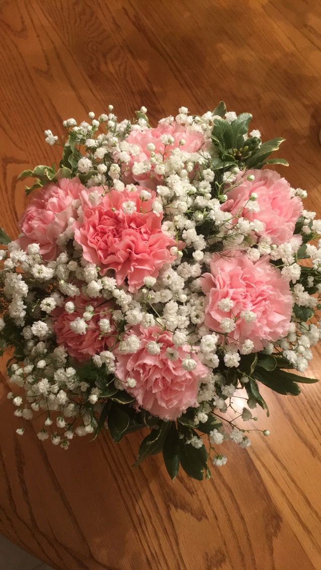 a bouquet of pink carnations and baby's breath on a wooden table