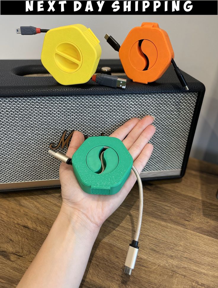 a hand holding a green and yellow object next to a blue and orange speaker with the words next day shipping on it