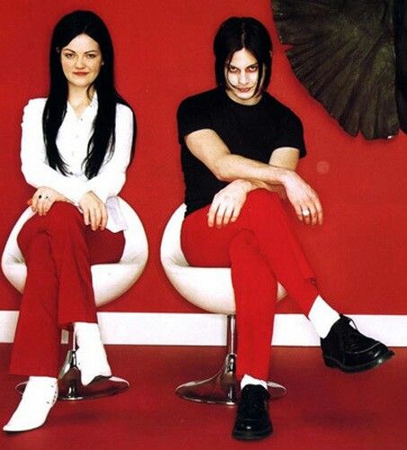 two people sitting on top of chairs in front of a red wall and black bird