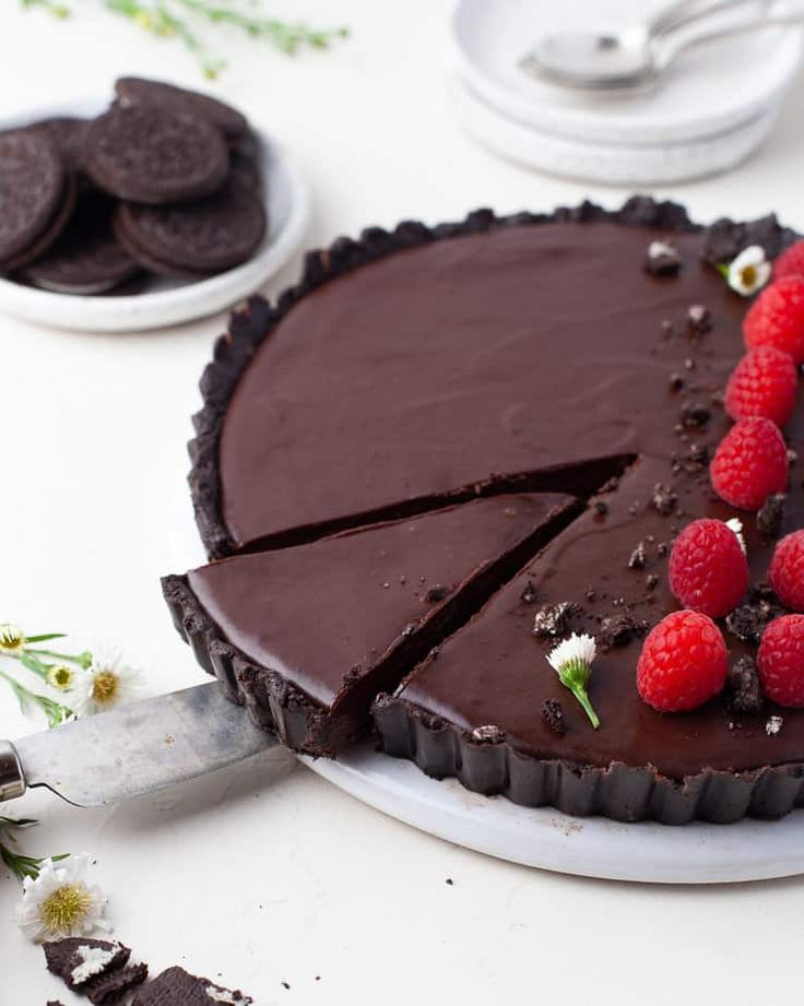 a chocolate tart with raspberries and oreo cookies on the side next to it