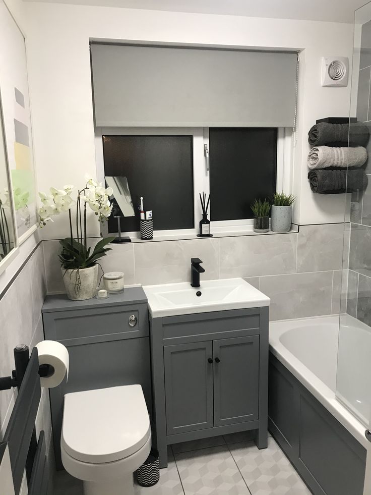 a white toilet sitting next to a bath tub under a window in a bathroom with gray cabinets